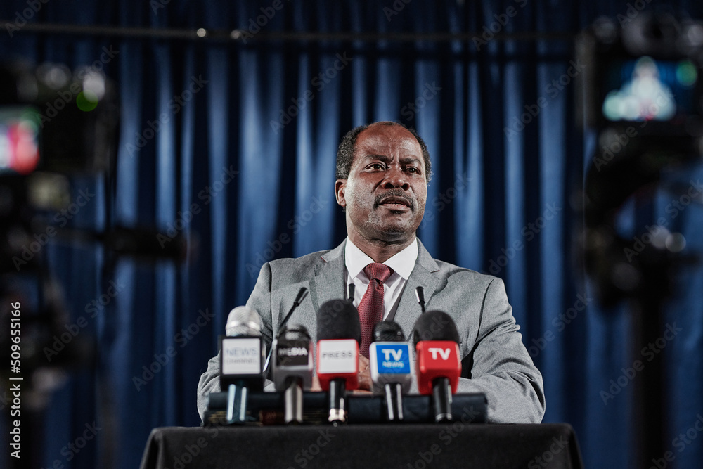 African mature politician standing at tribune with media microphones and giving an interview during press conference - obrazy, fototapety, plakaty 