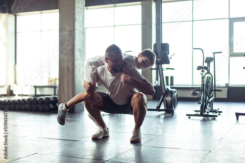 Healthy family concept. Father squats with his son on his shoulders in the gym. Fitness, sports, active lifestyle