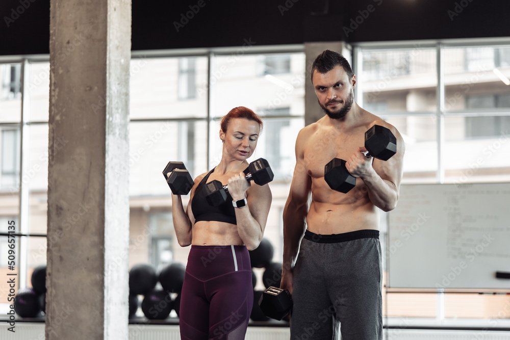 Athletic couple man and woman with dumbbells in their hands posing in gym