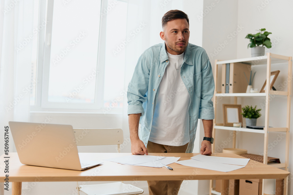 Thoughtful pensive handsome stylish young businessman deals with documents and papers for work project reclines on office table. Copy space for ad. Remote Job, Technology And Career Profession Concept