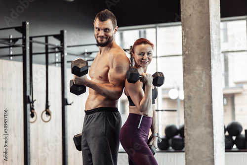 Athletic couple man and woman with dumbbells in their hands posing in gym