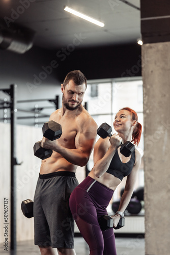 Athletic couple man and woman with dumbbells in their hands posing in gym