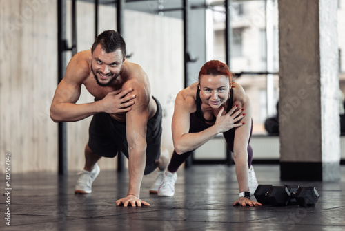 Athletic smiling couple man and woman do push-ups together in the gym. Healthy lifestyle