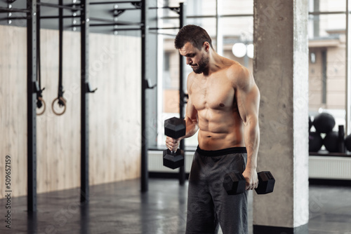 Athletic man with naked torso trains biceps with dumbbells in his hands Fototapete