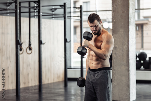 Fotobehang Athletic man with naked torso trains biceps with dumbbells in his hands