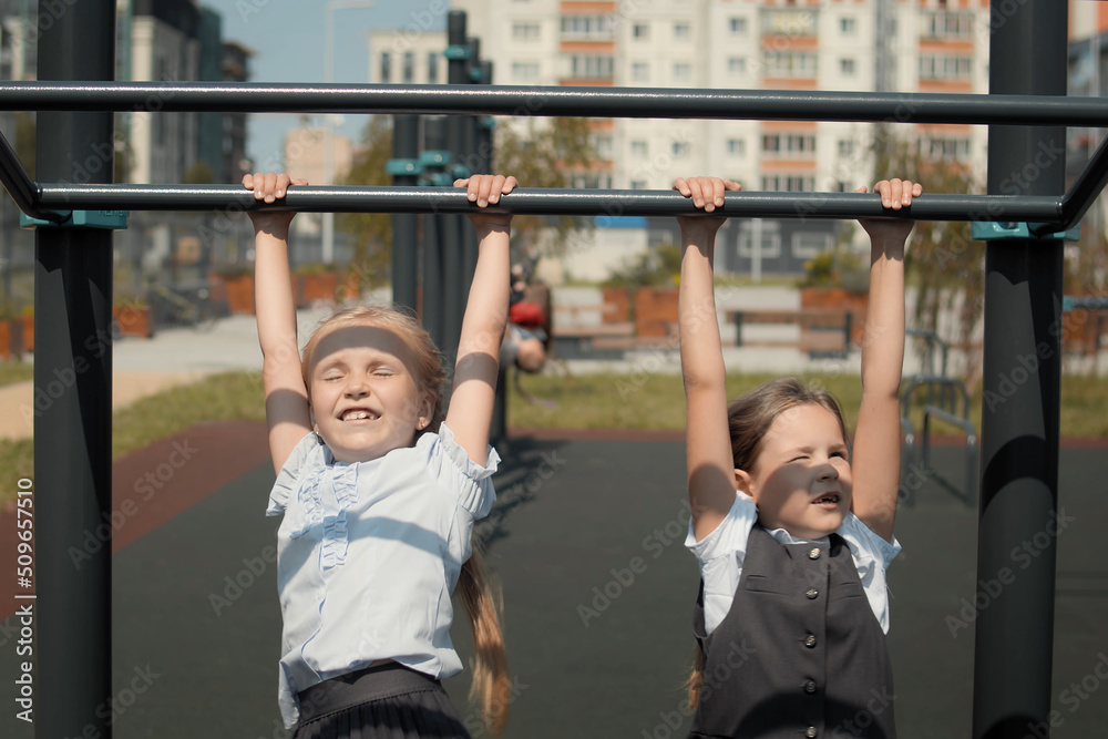 Obraz premium Two little schoolgirls jumping onto the monkey bars at a playground in schoolyard. Schoolmates wearing school uniform and play during school break.