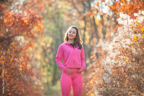 Portrait of a cute fitness woman in a pink sportswear in the autumn forest