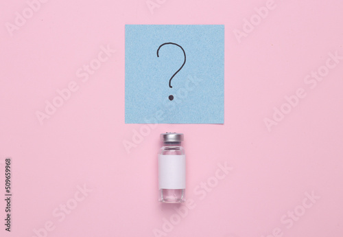 Medicine concept. Vaccine bottle with a question mark on a memo paper on a pink background. Top view photo