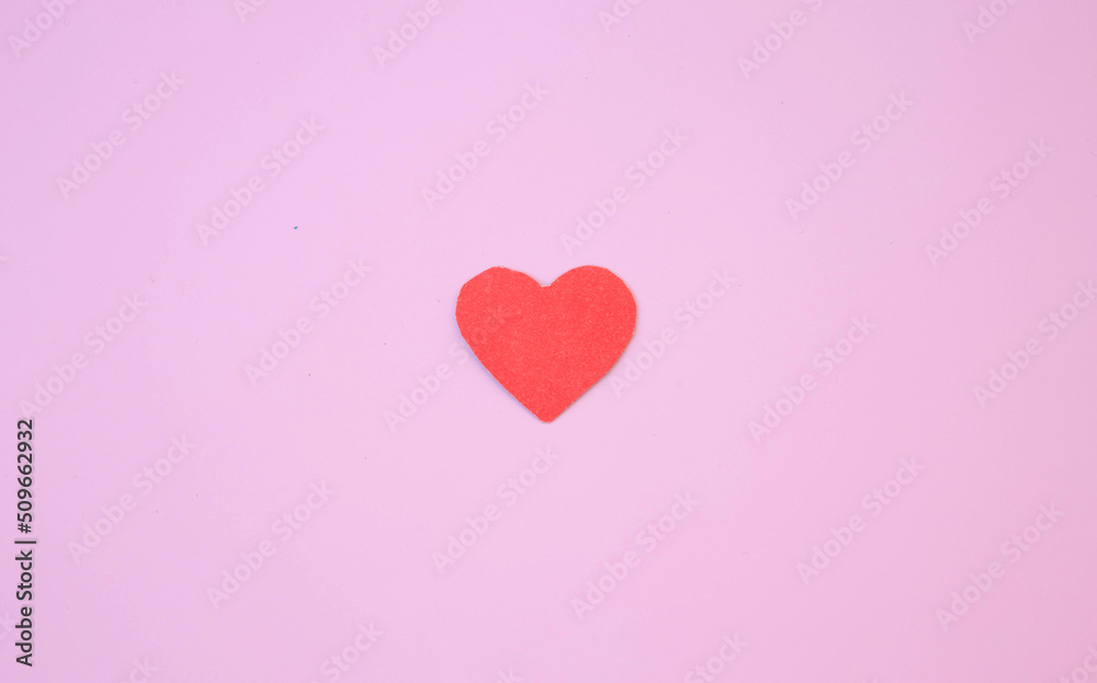 A red heart cut out of cardboard lies on a pink background