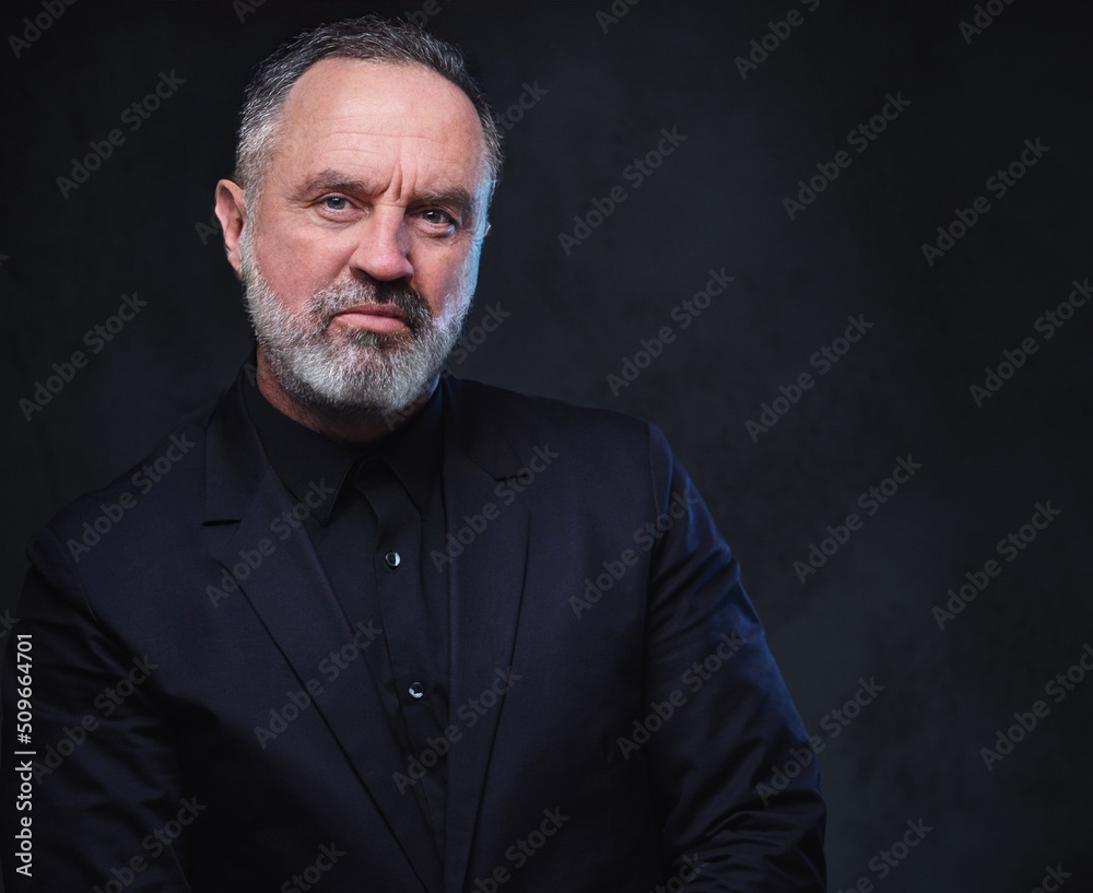 Portrait of handsome elderly dressed in black formal clothes with stylish hairstyle against dark background.
