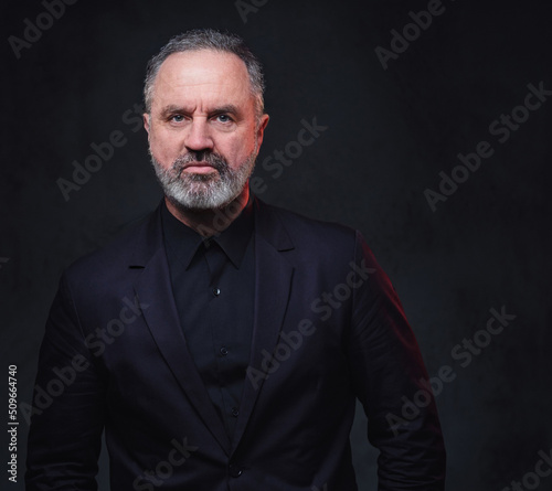 Portrait of handsome elderly dressed in black formal clothes with stylish hairstyle against dark background.