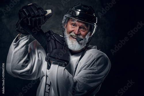 Studio shot of happy gray haired grandfather hockey player dressed in white sportswear. photo