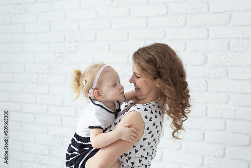 Mother holds her child with hearing aids and cochlear implants on white brick wall with copy space and place for advertising . Deaf and health concept