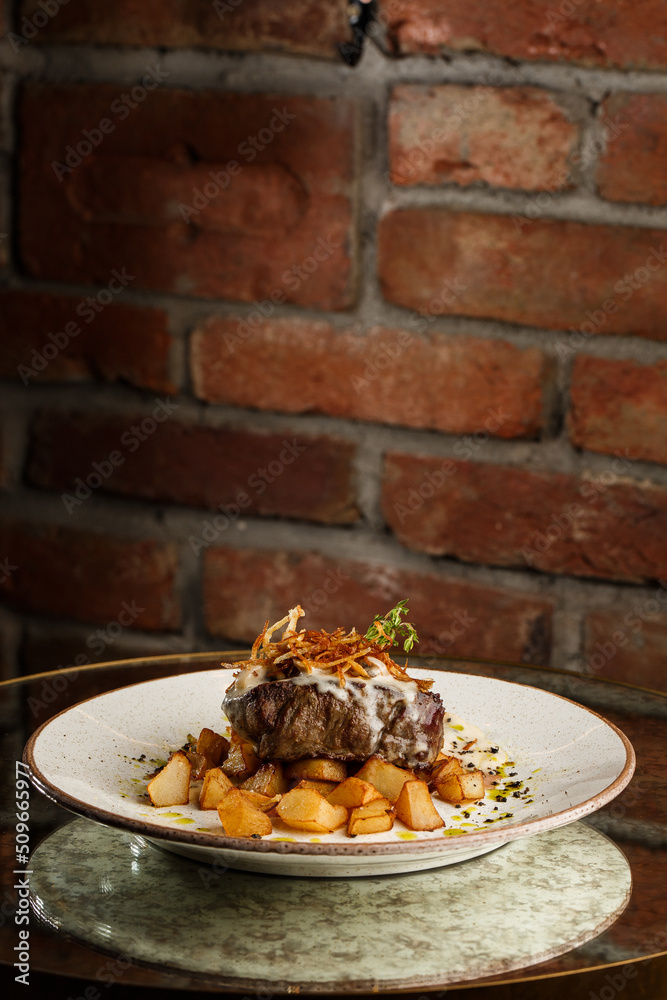 Grilled steak with baked golden potatoes served with crispy onion on top on a brick background. Delicious Recipe.