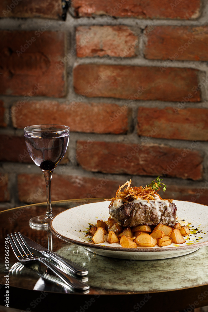 Grilled steak with baked golden potatoes served with crispy onion on top on a brick background. Delicious Recipe.