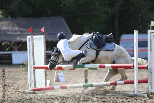 Unknown unidentified rider fall off her grey colored horse meanwhile riding in the outdoor arena. Equestrian sport background..