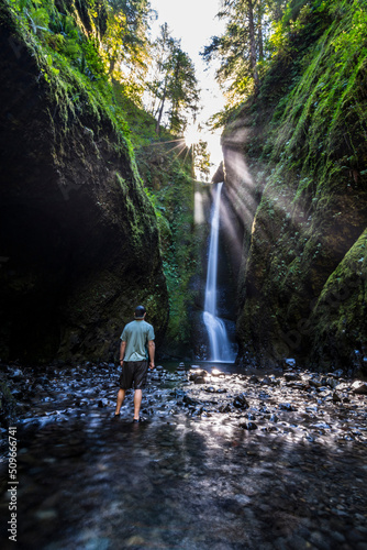 Adventurous athletic man standing in front of a waterfall in a river gorge.