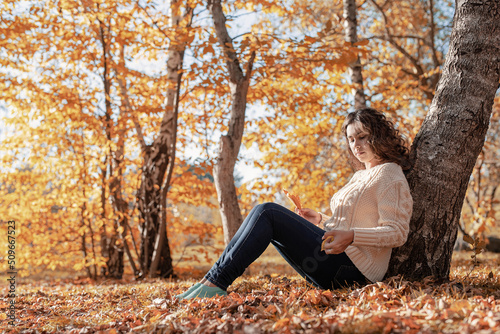 Young thoughtful woman sitting by the tree in autumn forest