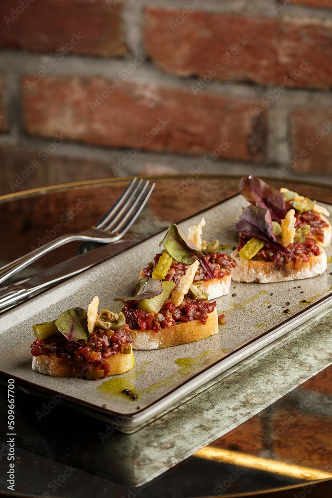 Four bruschettas with beef tartare on a plate, Crostini with Beef Tartare, beef Bruschetta, sandwich with raw gourmet beef.