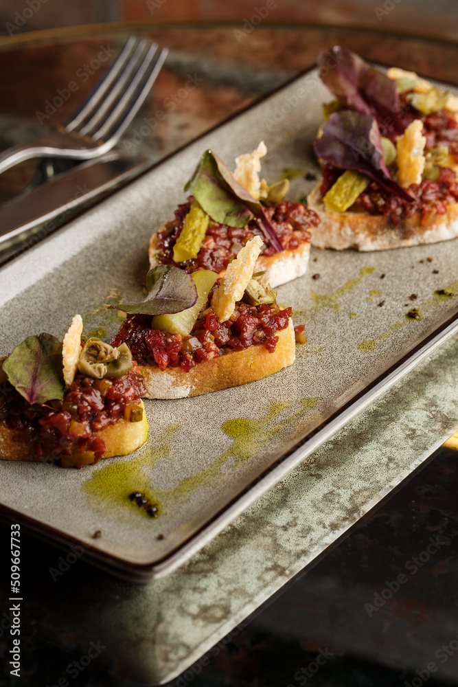 Four bruschettas with beef tartare on a plate, Crostini with Beef Tartare, beef Bruschetta, sandwich with raw gourmet beef.