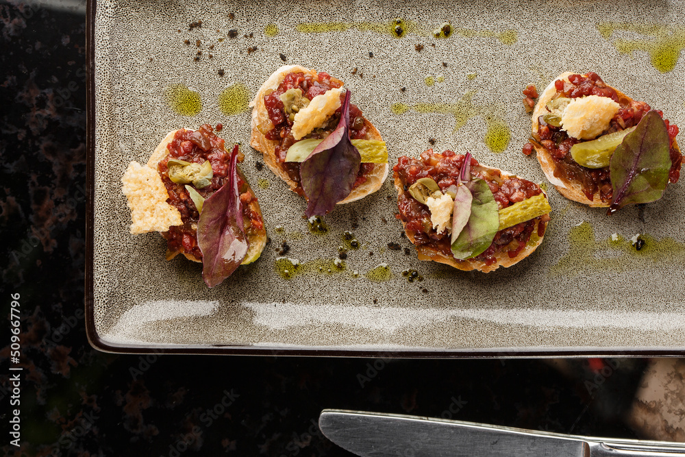 Four bruschettas with beef tartare on a plate, Crostini with Beef Tartare, beef Bruschetta, sandwich with raw gourmet beef.