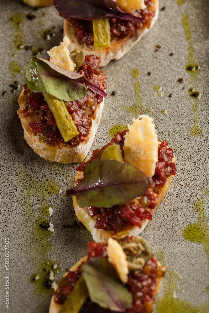 Four bruschettas with beef tartare on a plate, Crostini with Beef Tartare, beef Bruschetta, sandwich with raw gourmet beef.