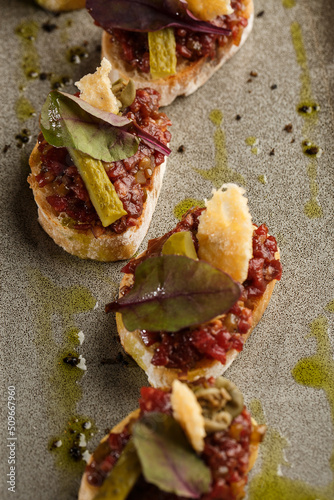 Obraz na płótnie Four bruschettas with beef tartare on a plate, Crostini with Beef Tartare, beef Bruschetta, sandwich with raw gourmet beef. w salonie