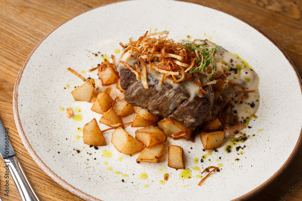 Grilled steak with baked golden potatoes served with crispy onion on top on a brick background. Delicious Recipe.