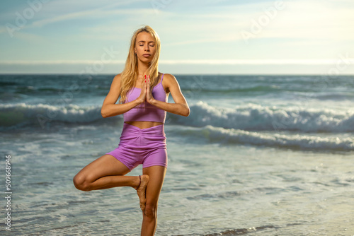 The girl practices yoga on the ocean coast. Download high resolution photo for social media. Idea for a fitness post.