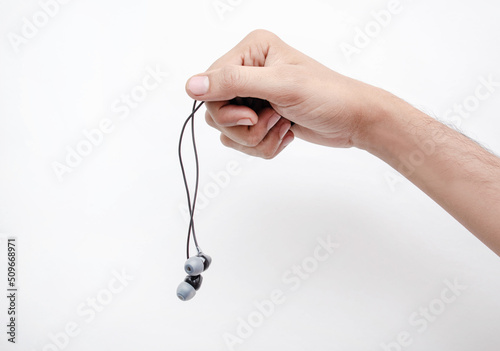 Mano de un hombre joven y delgado sosteniendo unos audifonos de cable color negro en un fondo blanco aislado