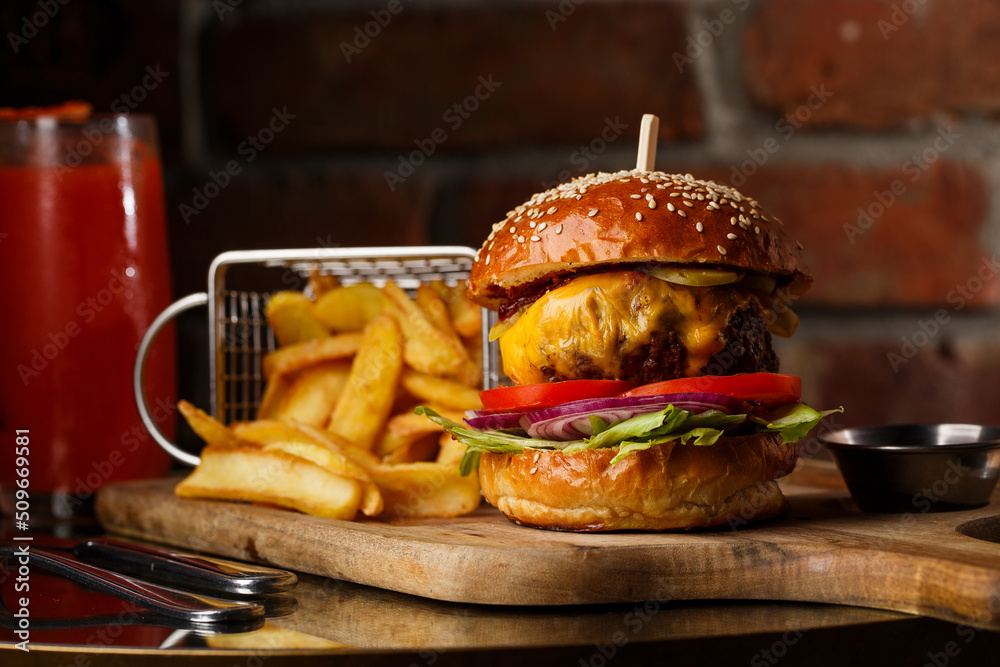 Big cheeseburger with french fries isolated on white background. Hamburger with beef patty onion, tomato, lettuce pickles, melted cheddar, mustards, tomato jam, mayo