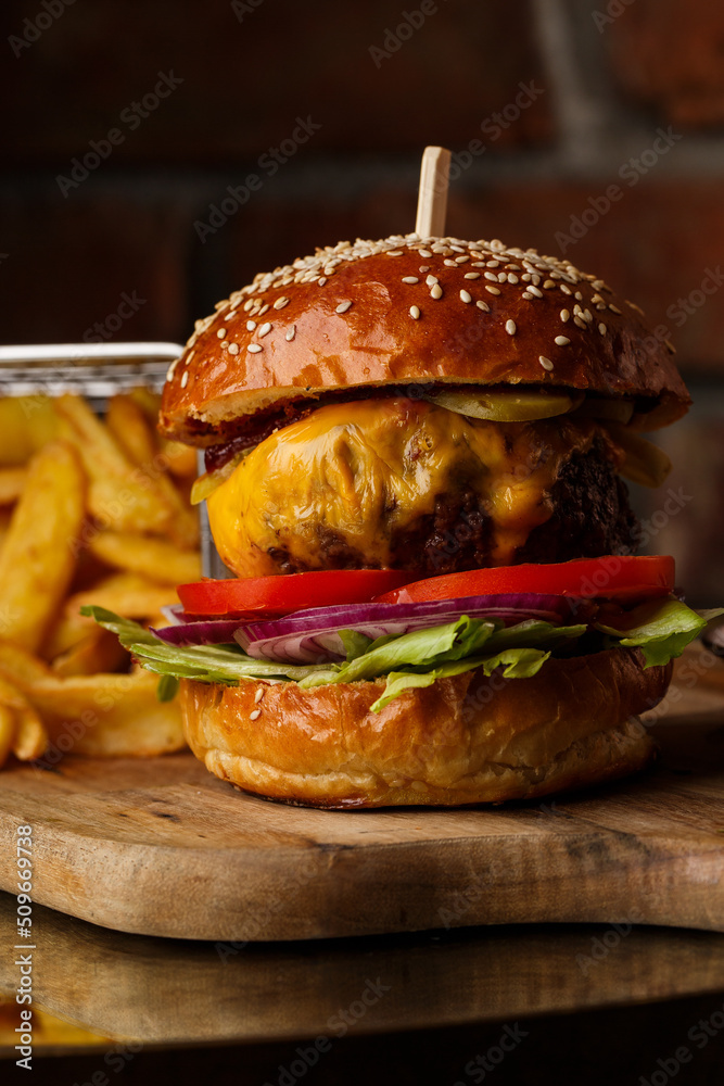 Big cheeseburger with french fries isolated on white background. Hamburger with beef patty onion, tomato, lettuce pickles, melted cheddar, mustards, tomato jam, mayo