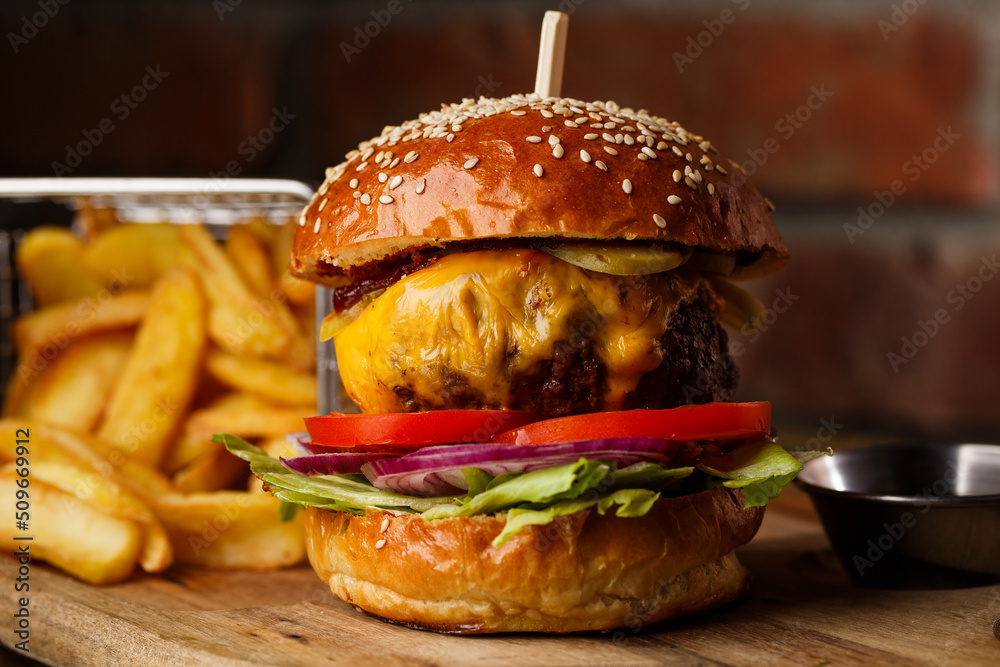 Big cheeseburger with french fries isolated on white background. Hamburger with beef patty onion, tomato, lettuce pickles, melted cheddar, mustards, tomato jam, mayo
