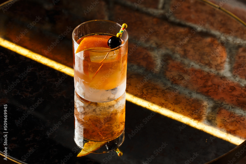 Crystal glass with bright cold alcoholic cocktail decorated with orange zest. Blurred background. Negroni cocktail.