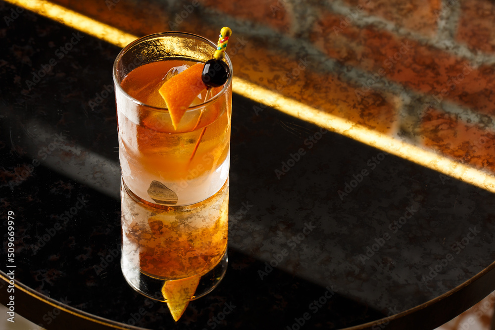 Crystal glass with bright cold alcoholic cocktail decorated with orange zest. Blurred background. Negroni cocktail.