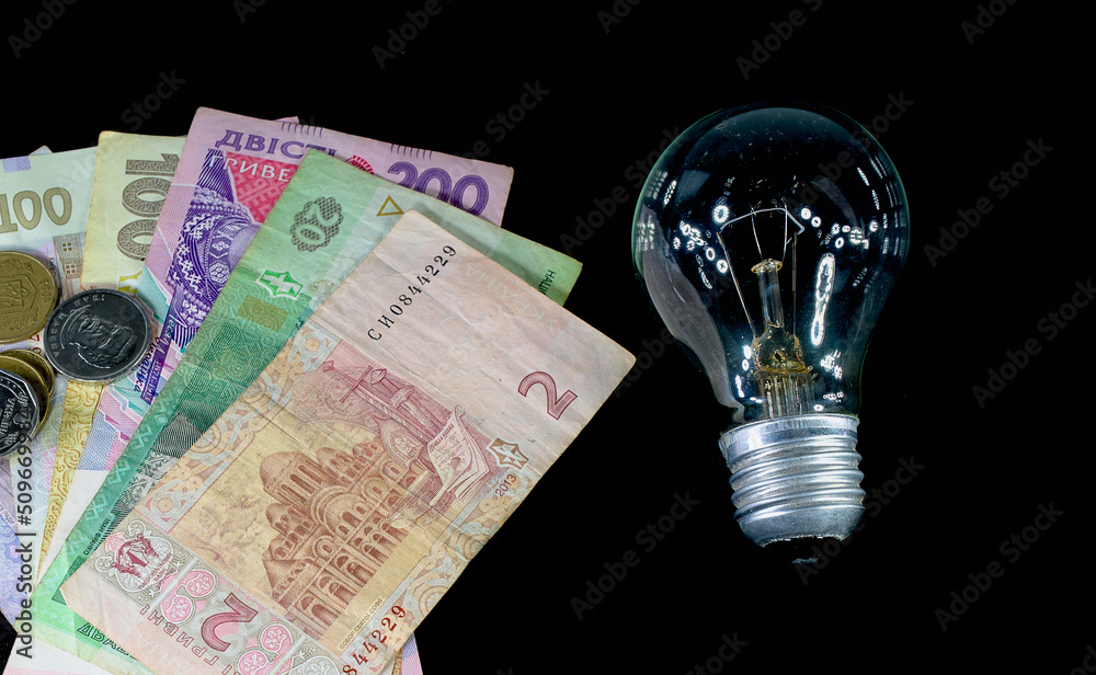 electricity lamp and Ukrainian hryvnia close up on a black background. The concept of the cost of electricity and energy resources electricity lamp and Ukrainian hryvnia close up on a black background. The concept of the cost of electricity and energy resources