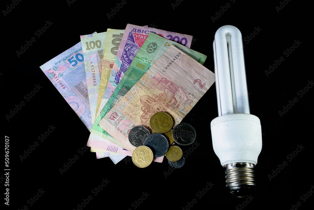Economy lamp and Ukrainian hryvnia close up on a black background. The concept of the cost of electricity and energy resources Economy lamp and Ukrainian hryvnia close up on a black background. The concept of the cost of electricity and energy resources