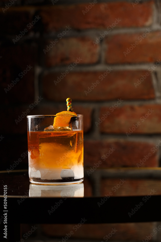 Crystal glass with bright cold alcoholic cocktail decorated with orange zest. Blurred background. Negroni cocktail.