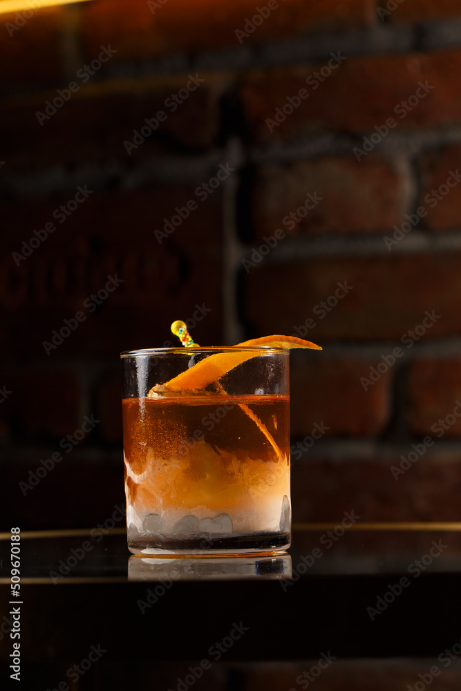 Crystal glass with bright cold alcoholic cocktail decorated with orange zest. Blurred background. Negroni cocktail.