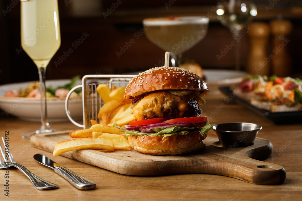 Big cheeseburger with french fries isolated on white background. Hamburger with beef patty onion, tomato, lettuce pickles, melted cheddar, mustards, tomato jam, mayo