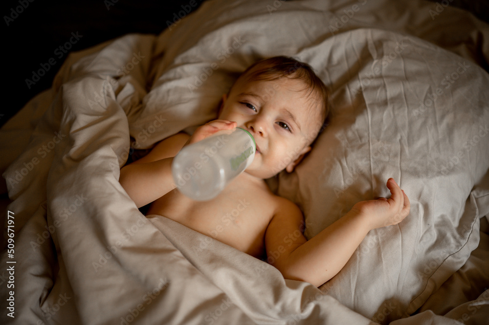 baby lies in bed with a bottle in his hands
