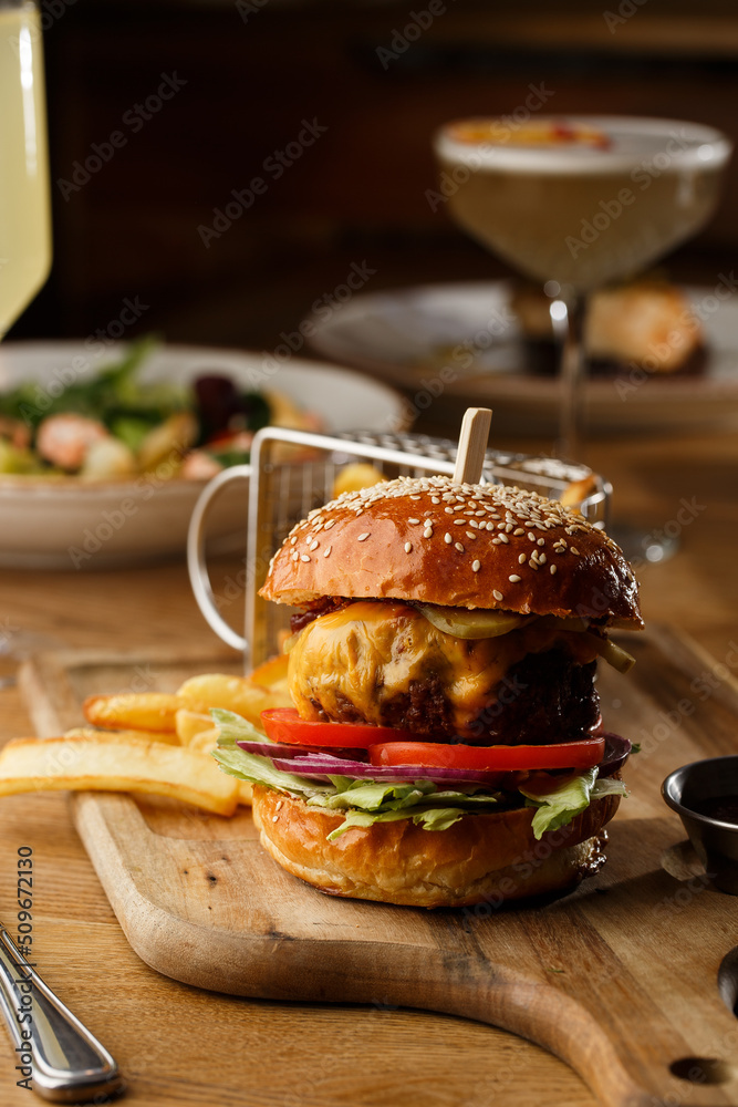 Big cheeseburger with french fries isolated on white background. Hamburger with beef patty onion, tomato, lettuce pickles, melted cheddar, mustards, tomato jam, mayo