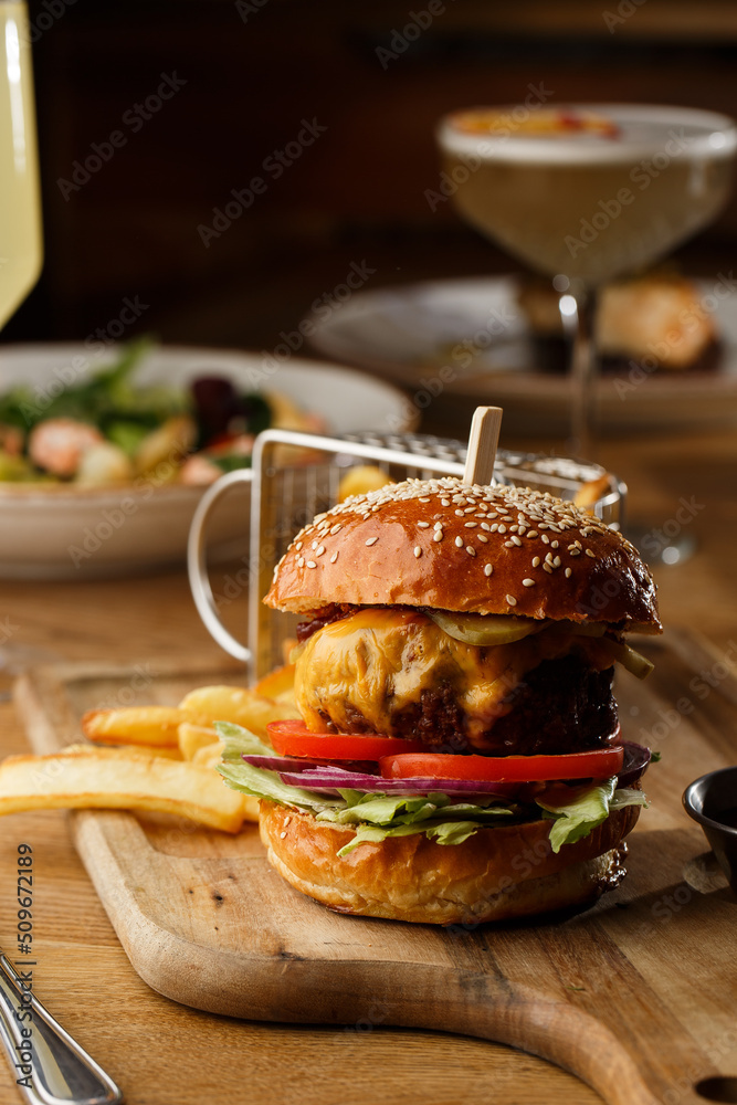 Big cheeseburger with french fries isolated on white background. Hamburger with beef patty onion, tomato, lettuce pickles, melted cheddar, mustards, tomato jam, mayo
