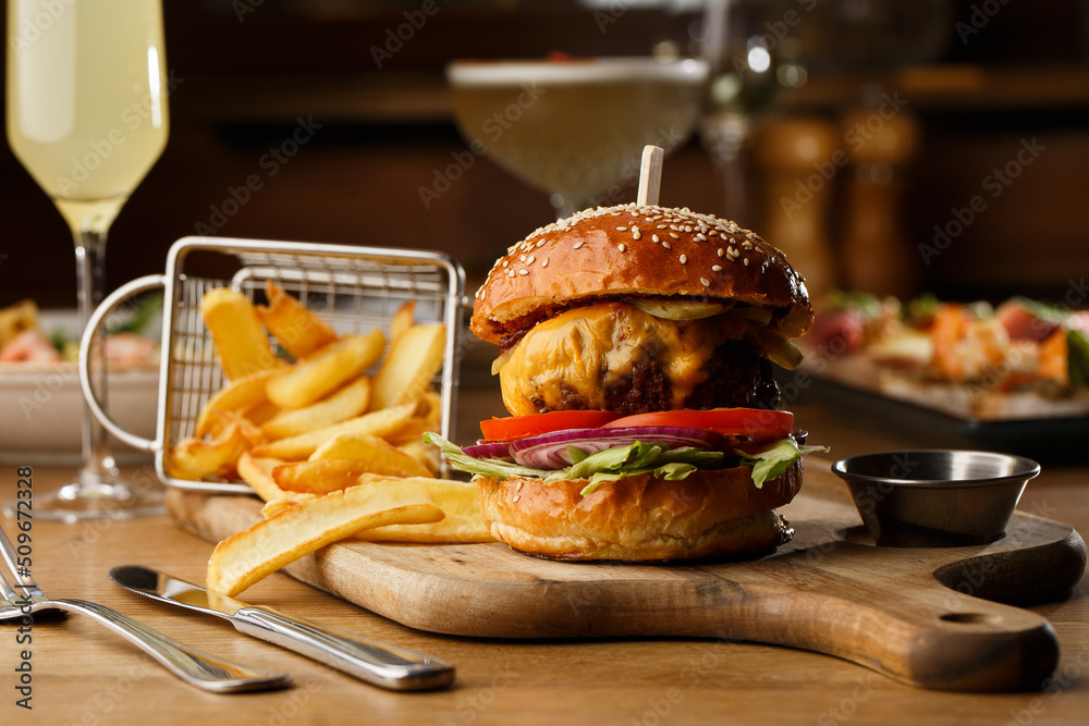 Big cheeseburger with french fries isolated on white background. Hamburger with beef patty onion, tomato, lettuce pickles, melted cheddar, mustards, tomato jam, mayo