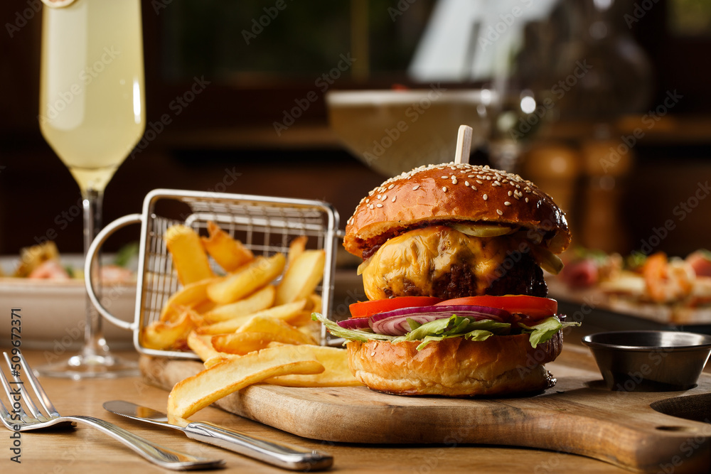 Big cheeseburger with french fries isolated on white background. Hamburger with beef patty onion, tomato, lettuce pickles, melted cheddar, mustards, tomato jam, mayo