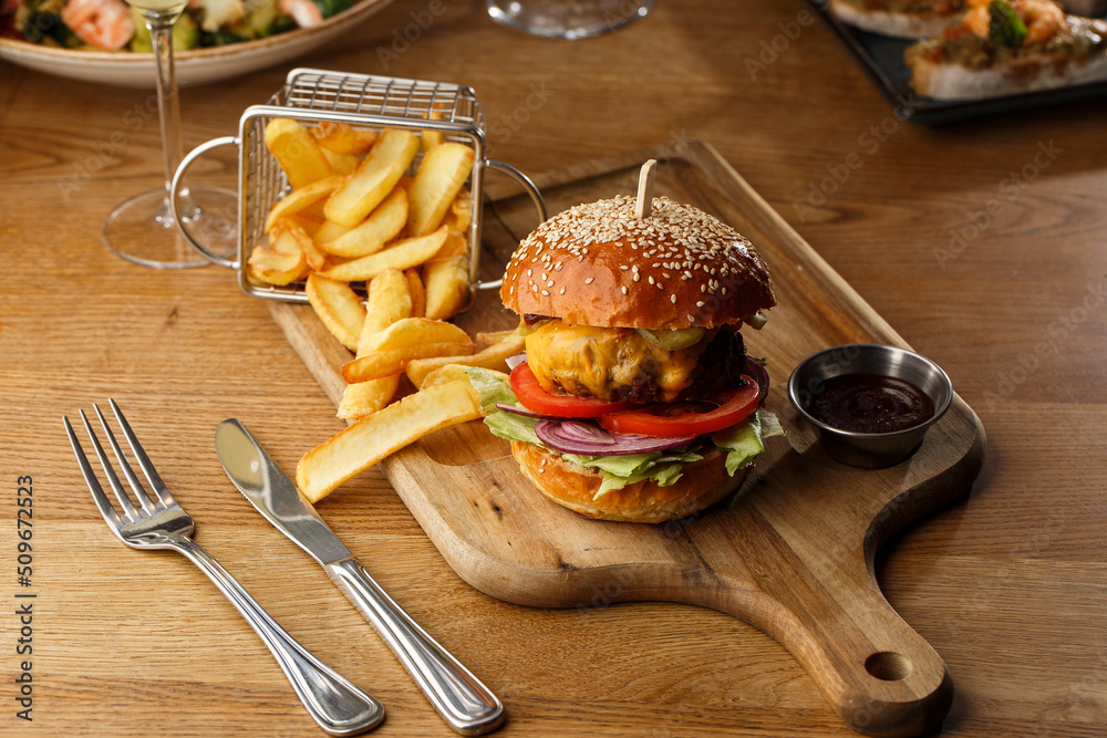 Big cheeseburger with french fries isolated on white background. Hamburger with beef patty onion, tomato, lettuce pickles, melted cheddar, mustards, tomato jam, mayo