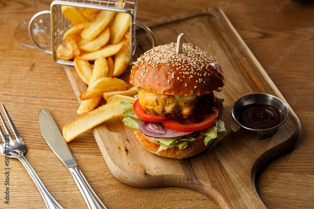 Big cheeseburger with french fries isolated on white background. Hamburger with beef patty onion, tomato, lettuce pickles, melted cheddar, mustards, tomato jam, mayo
