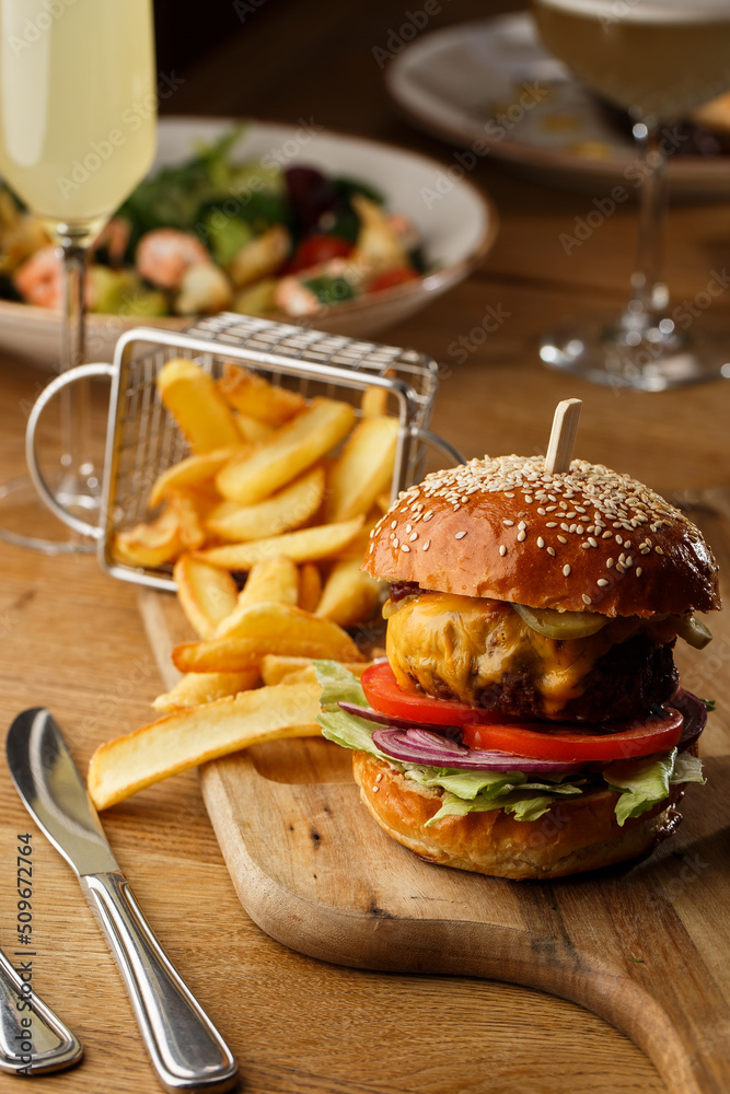 Big cheeseburger with french fries isolated on white background. Hamburger with beef patty onion, tomato, lettuce pickles, melted cheddar, mustards, tomato jam, mayo