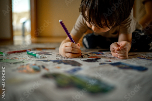 boys draw with colored pencils, a boy of Asian appearance paints a coloring book