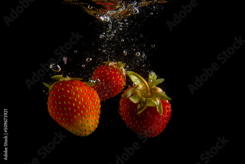 ripe strawberries fall into the water  raising splashes and air bubbles